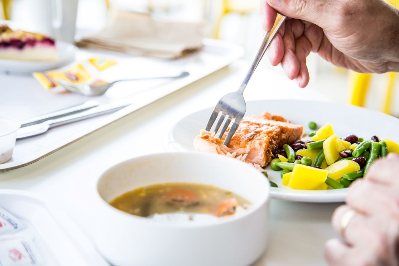 Adult woman over 55 eating a salmon and vegetable meal representing foods for knee health over 55 that help reduce OA pain.