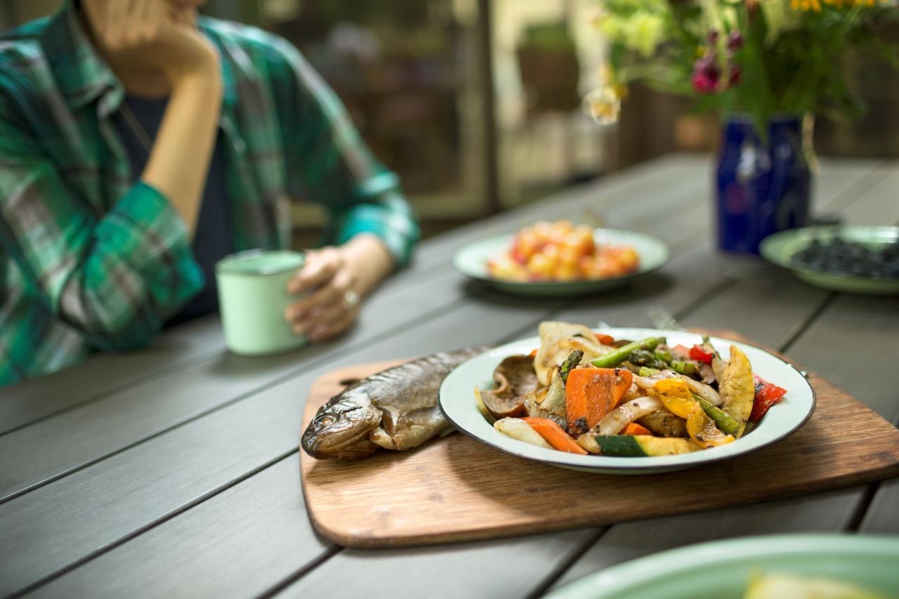 Adult woman over 55 at a dinner table with a Mediterranean-style meal of grilled fish and vegetables supporting knee health through diet.