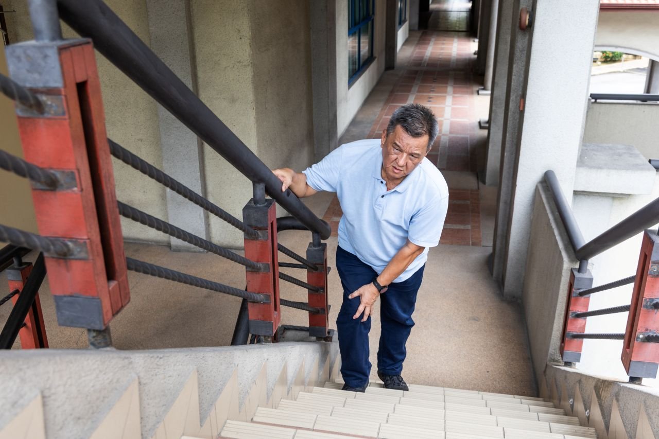 Adult man over 55 at the bottom of outdoor stairs with a cautious posture showing how elevated inflammation affects walking capacity and mobility in older adults.
