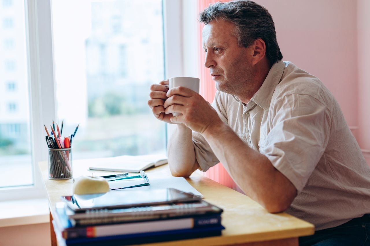 Adult man over 55 at a kitchen table in the morning with a journal reflecting on his mindset for walking with knee pain before starting the day.