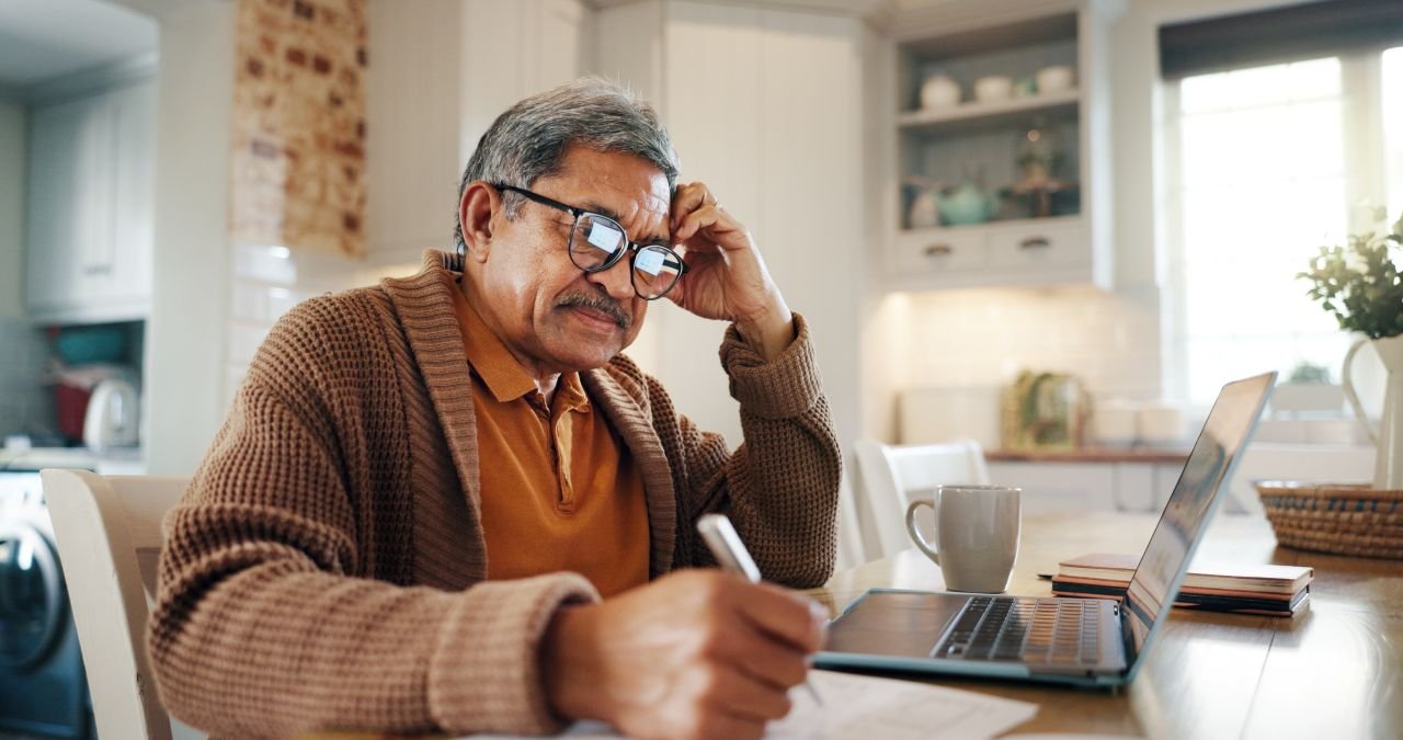 Adult man over 55 writing in a notebook at a kitchen table representing the P.I.S.T. self-talk practice that supports mindset for walking with knee pain.