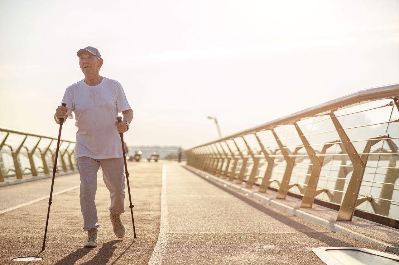 Adult man over 60 walking a long park path with poles illustrating how consistent pole walking builds walking distance over time for adults with knee pain.