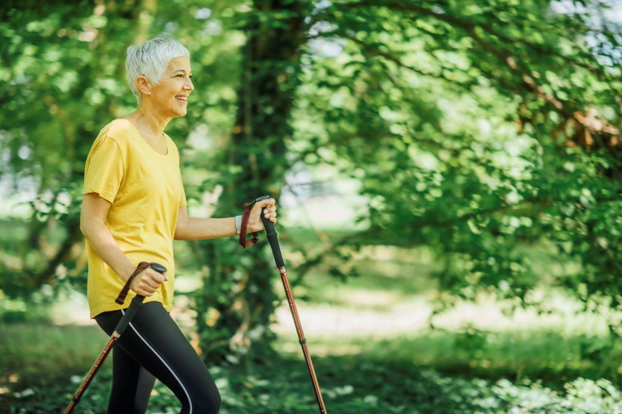 Adult woman over 60 walking on a park path with poles illustrating how walking poles for knee pain over 60 support movement and balance.